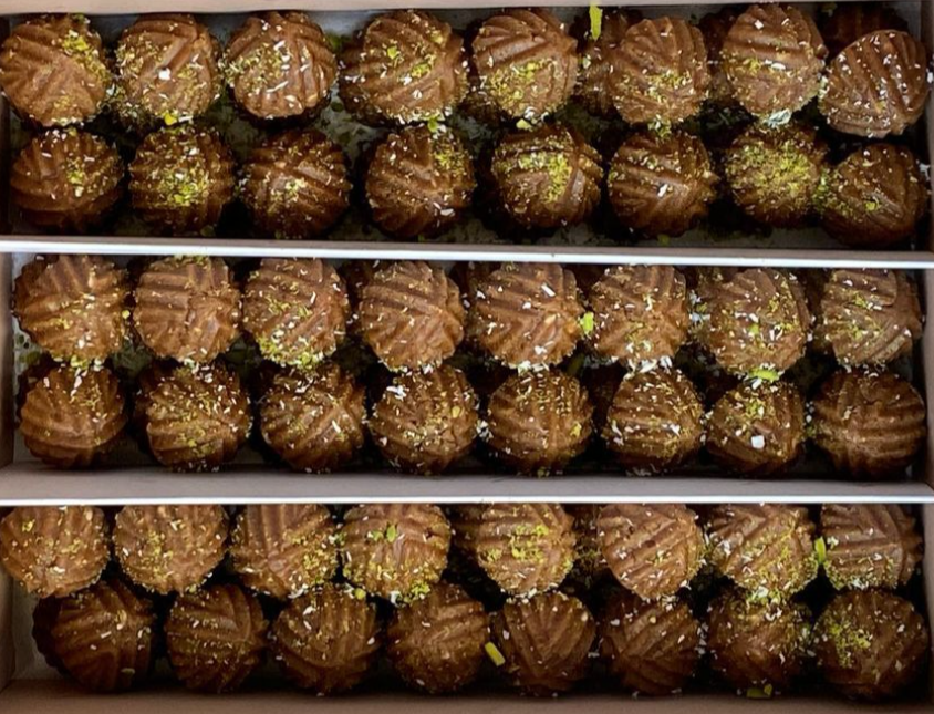 A box of bakery cookies with a golden-brown color and green sprinkles on top, arranged in rows.